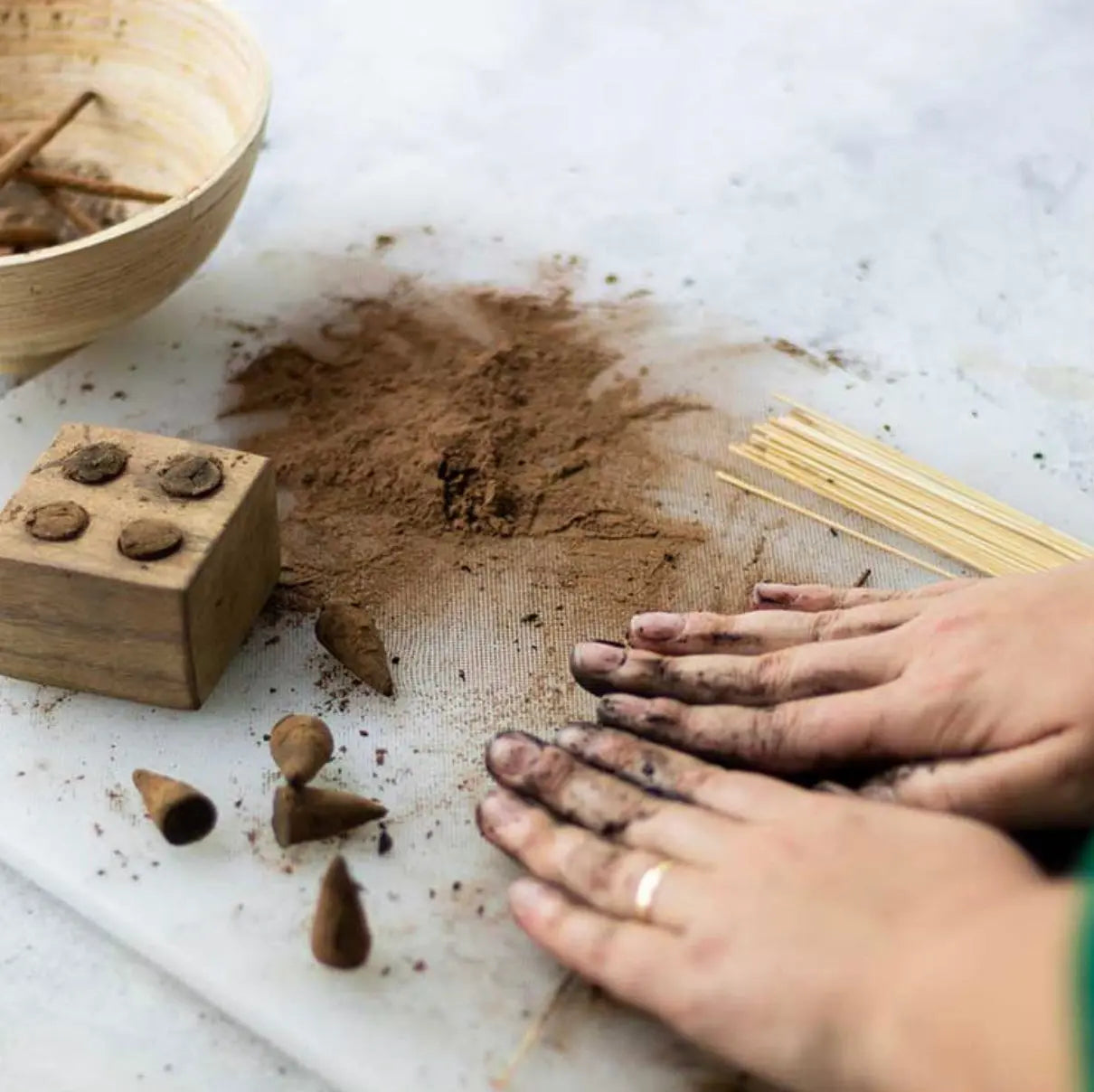 Handcrafting DIY Patchouli incense cones and sticks with brown powder, wooden mold, and bamboo sticks on marble surface