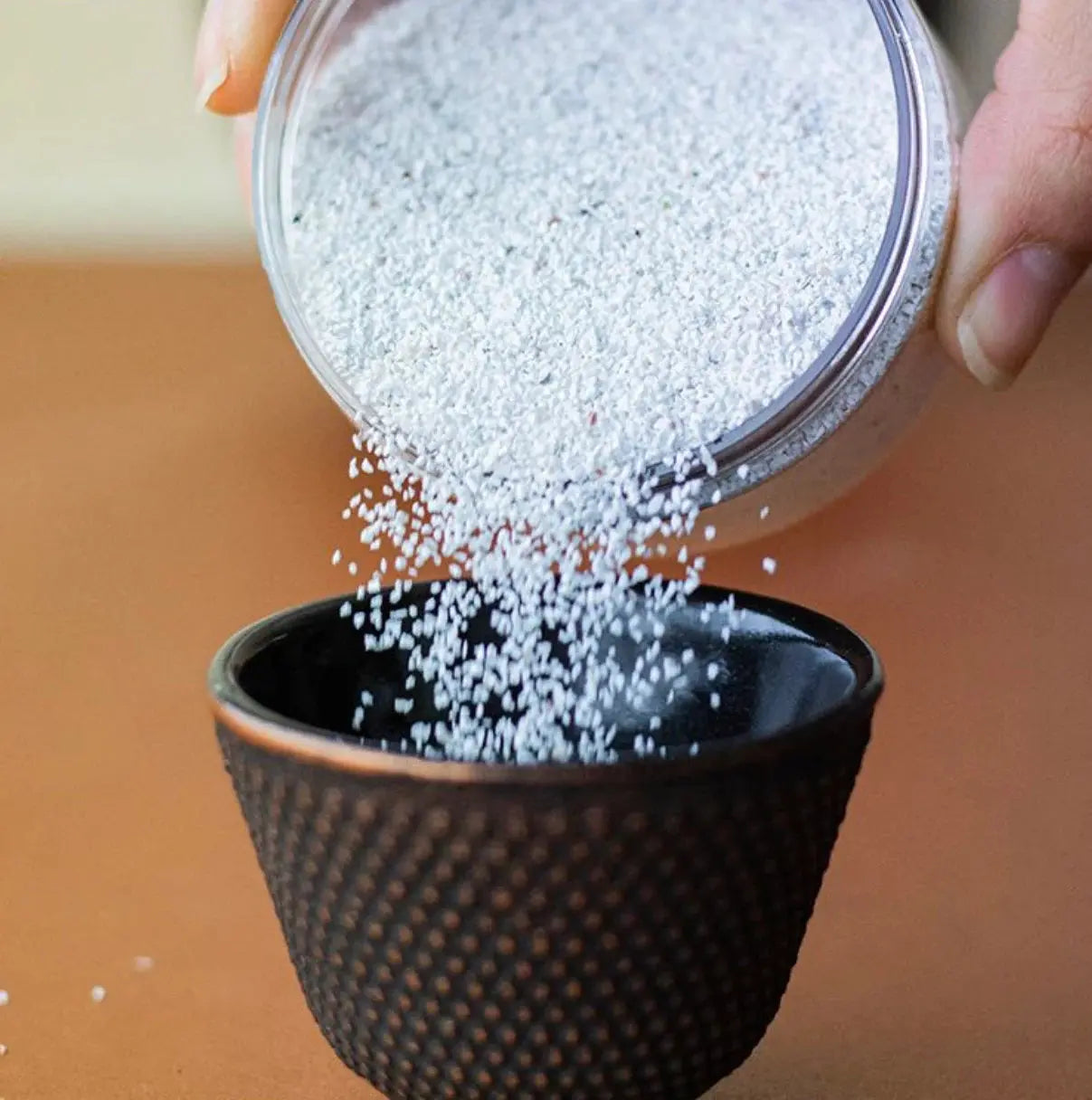 White Sable Blanc incense sand being poured into a black textured burner bowl, showing fine granular texture