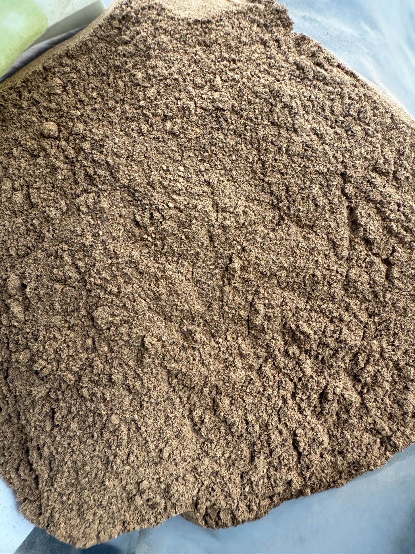 Finely ground Ashwagandha powder 50g shown in natural brown color with granular texture on light blue surface
