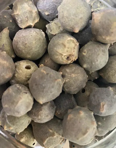 Closeup of Afss Tanin Aleppo oak galls, 100g package of natural round dark grey balls used for hair dye and natural coloring. Traditional Middle Eastern tannin-rich plant material shown in detailed texture.