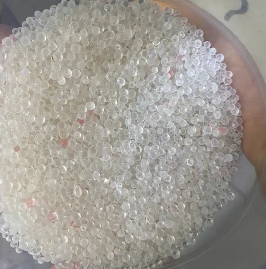 Al hikma 30g hekma mahkouma hakma: Small translucent round crystals or beads in a circular container, showing a dense collection of white to clear granules with subtle pink tints scattered throughout. Product appears in a plastic or glass dish with distinct spherical particles.