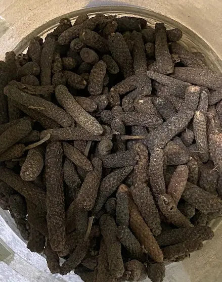 Dar el felfel long pepper spice in dark brown elongated pods shown in glass container, traditional Java pepper